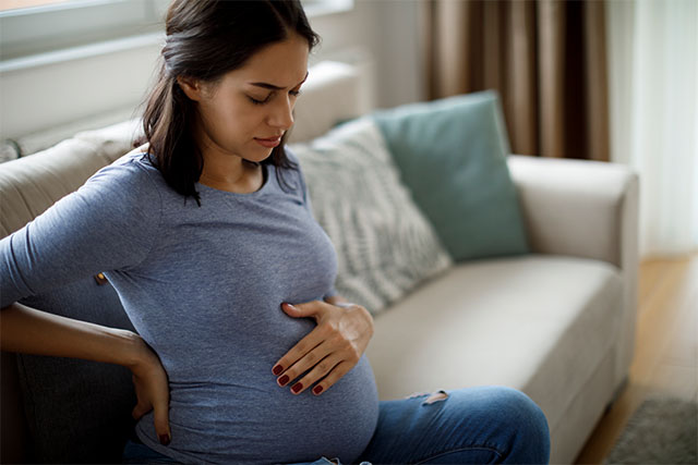 فردی که حامله میباشد بر روی مبل نشسته است و دست خود را به کمر و شکم گذاشته است