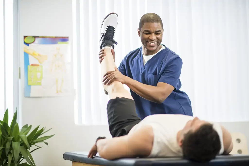 فرد فیزیوتراپیستی که در حال درمان کردن پای فردی که بر روی تخت دراز کشیده است