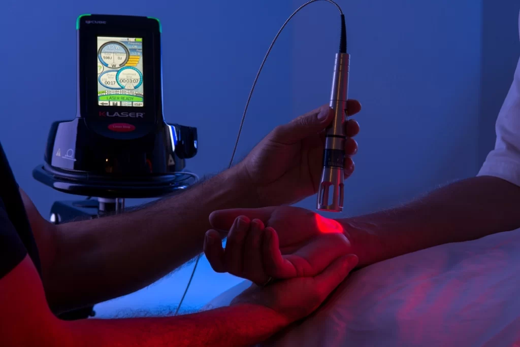 اتاق تاریکی که بیمار بر روی تخت دراز کشیده و دکتر درحال درمان آن فرد با دستگاه لیزر است