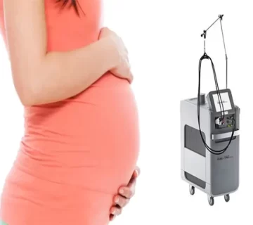 زن بارداری که لباس صورتی بر تن دارد و در کنار دستگاه لیزر ایستاده است