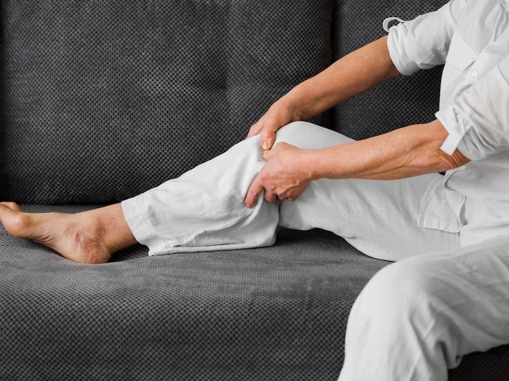 درمان پا درد از زانو به پایین - مرد سفیدپوش نشسته بر روی مبل دست ها بر روی زانو