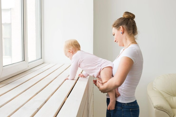 کمر درد بعد از زایمان - زن با کودک به بغل ایستاده کنار پنجره 