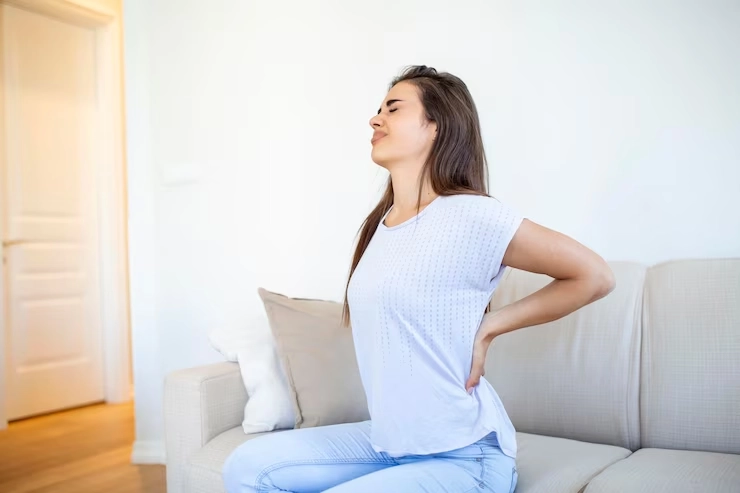 علت کمر درد در زنان - زن با کمردرد نشسته بر روی مبل 