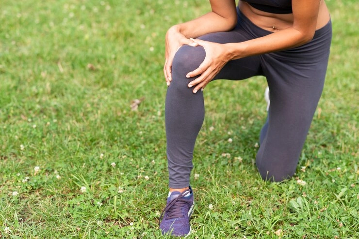 علت درد ران و ساق پا - شخص با درد زانو در حالی که روی چمن ها خم شده و با دستانش زانوی سمت راست را گرفته .