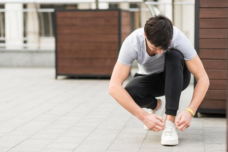  گرفتگی عضلات - مرد در حال خم شدن و بستن بند کفش کتونی